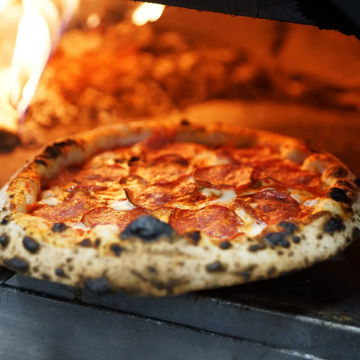 A pizza coming out of a wood-fired oven