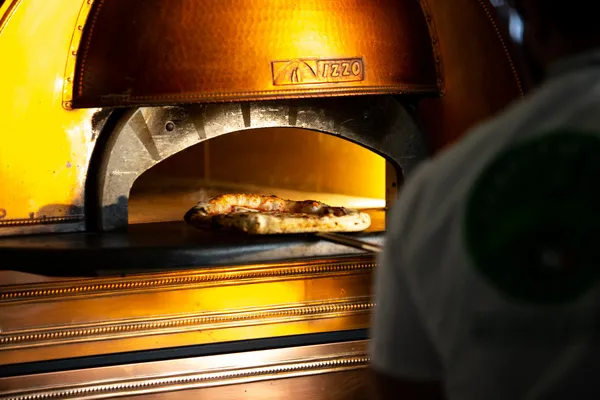 A pizza bakes on the floor of a glowing copper Izzo wood-fired oven at Pizzeria Luca in Helsinki.