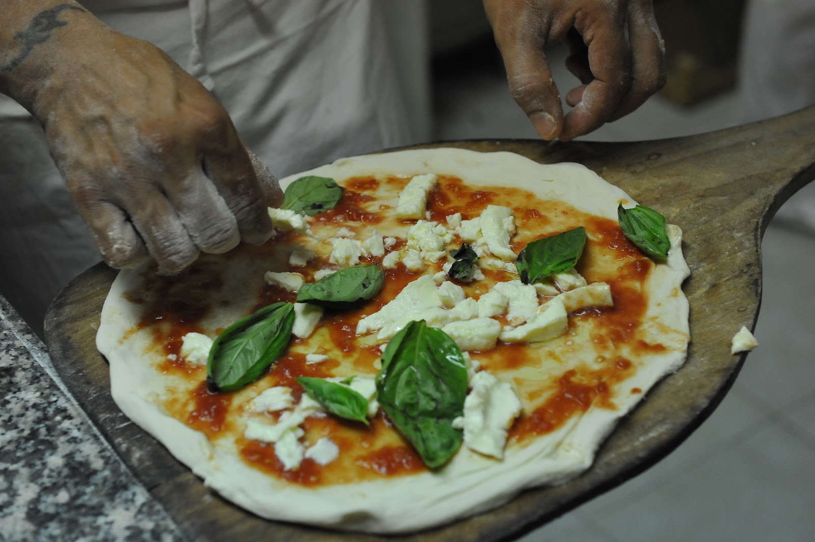 A pizzaiolo finishing a Margherita with fresh basil, mozzarella, and tomato sauce at Pizzeria Brandi in Naples.