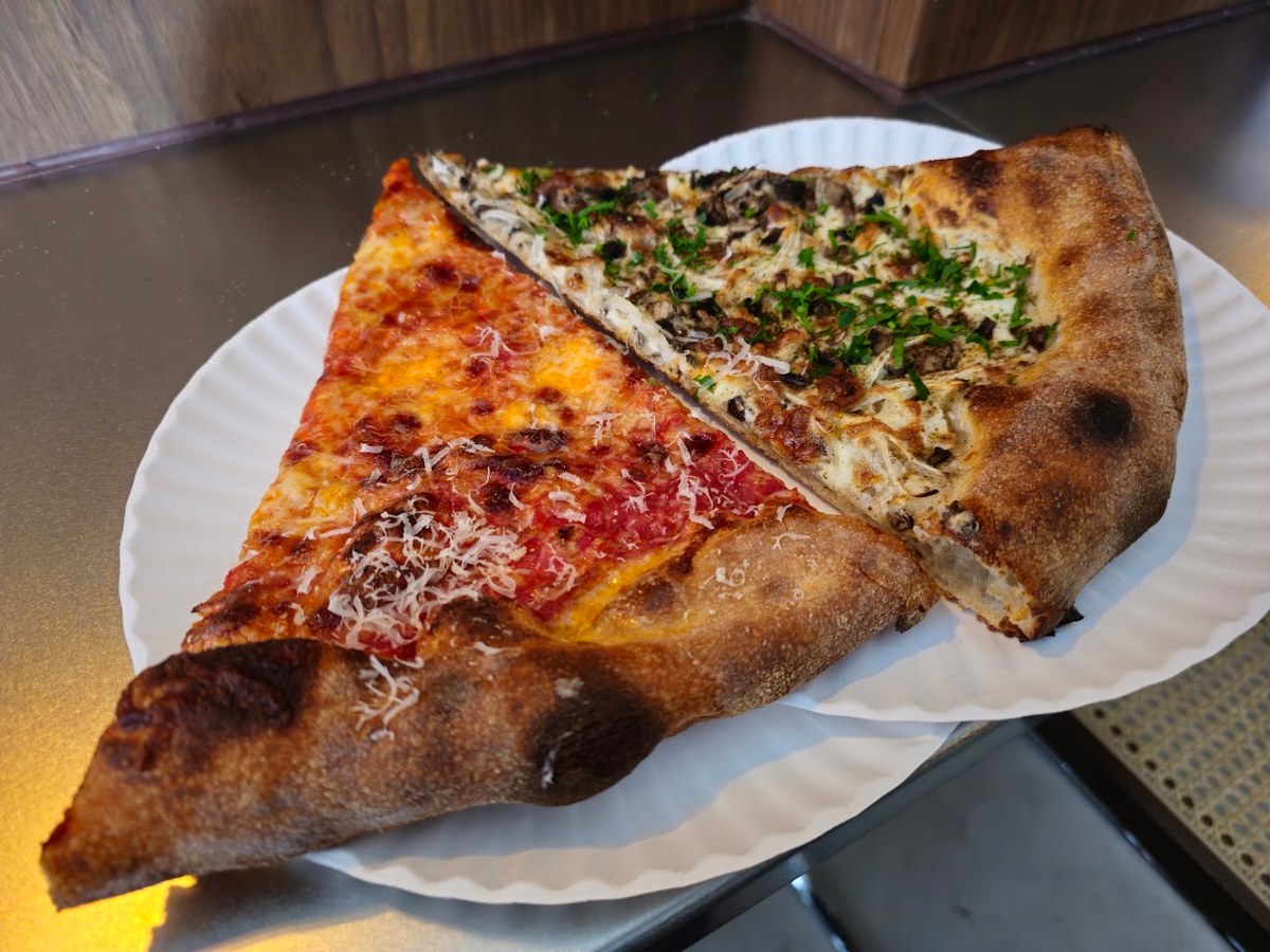 Two sourdough pizza slices on a paper plate at Ceres in New York, one with tomato and grated cheese, one white with mushrooms, onions and herbs.