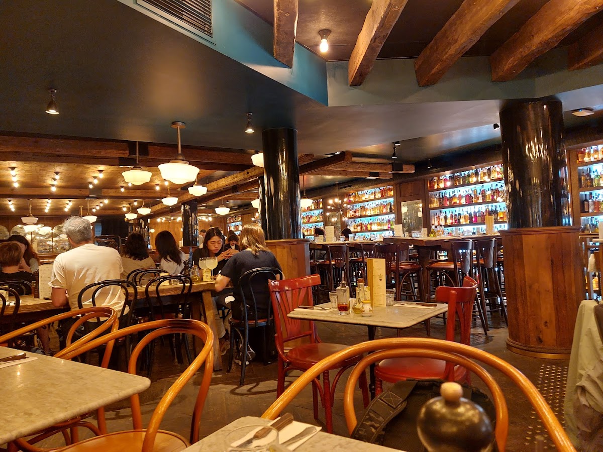 Pizzeria Popolare dining room in central Paris with wooden beams, pendant lights, and bottle-lined shelves.